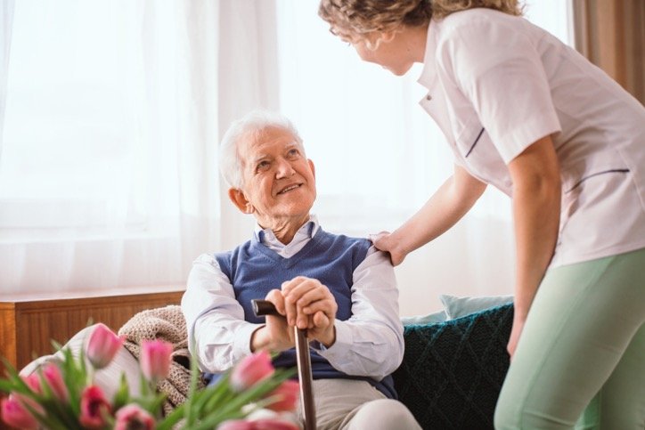 senior man with a walking stick being comforted by nurse in the picture