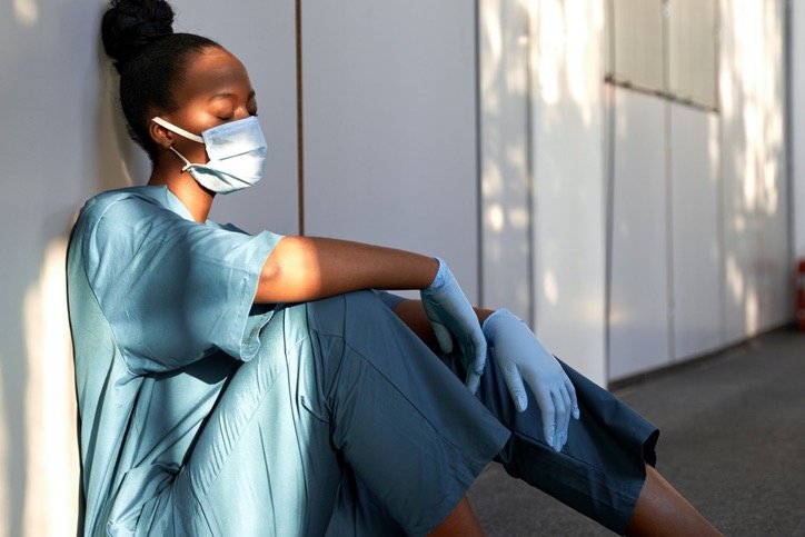 tired exhausted female african scrub nurse wears face mask blue on picture